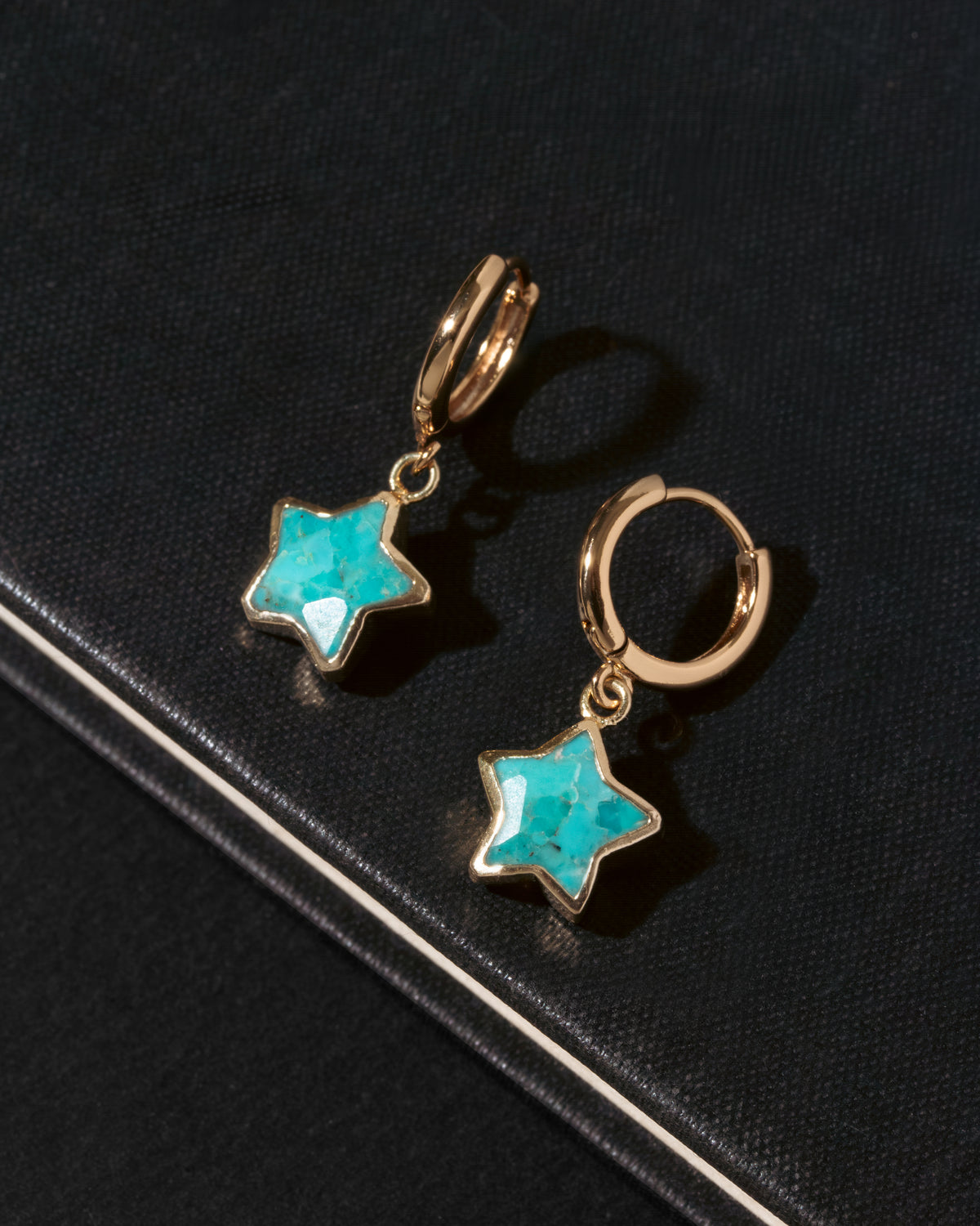 A pair of gold hoop earrings with dangling star-shaped turquoise stones.