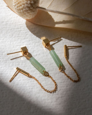 Gold double pierced earrings with cylindrical Green Aventurine charms on a white textured surface.