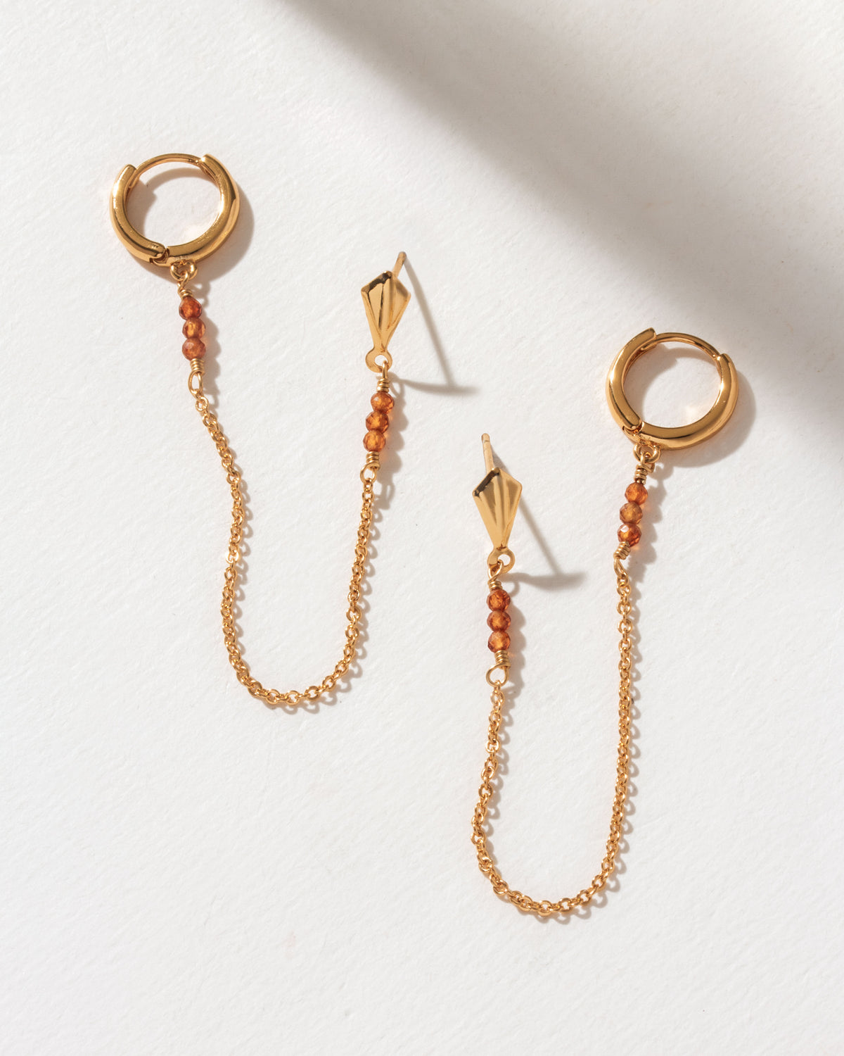 Two gold Cascades Double Pierced Hoop Earrings with Spessartite Garnet gemstone accents on a white background.