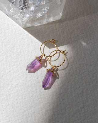 Gold hoop earrings with purple amethyst gemstone pendants on a white surface