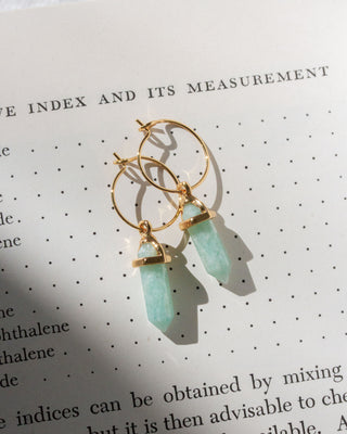 Gold hoop earrings with green amazonite gemstones on a book page