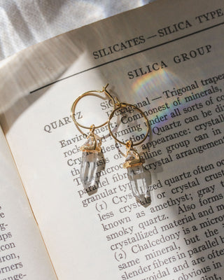Gold hoop earrings with clear quartz gemstones on an open book