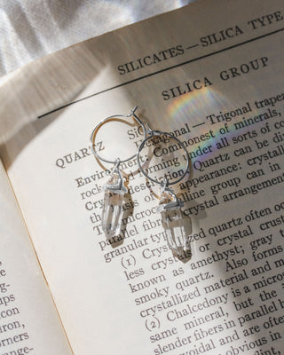 A pair of silver hoop earrings with clear quartz crystal charms.