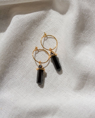 Gold hoop earrings with black  onyx cylindrical beads on a light fabric background