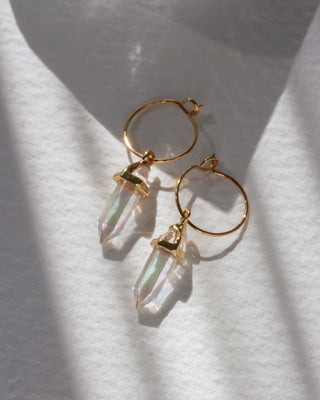 Gold hoop earrings with AB clear quartz pendants on a white fabric background