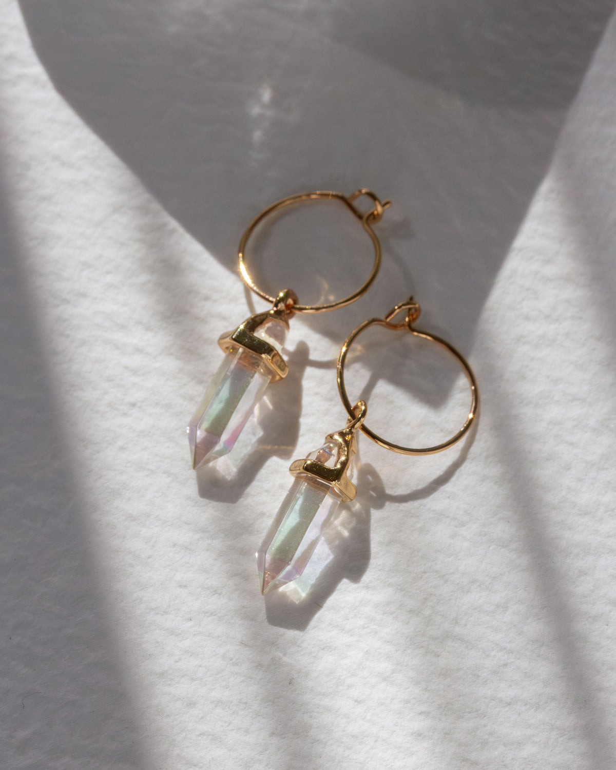 Gold hoop earrings with AB clear quartz pendants on a white fabric background