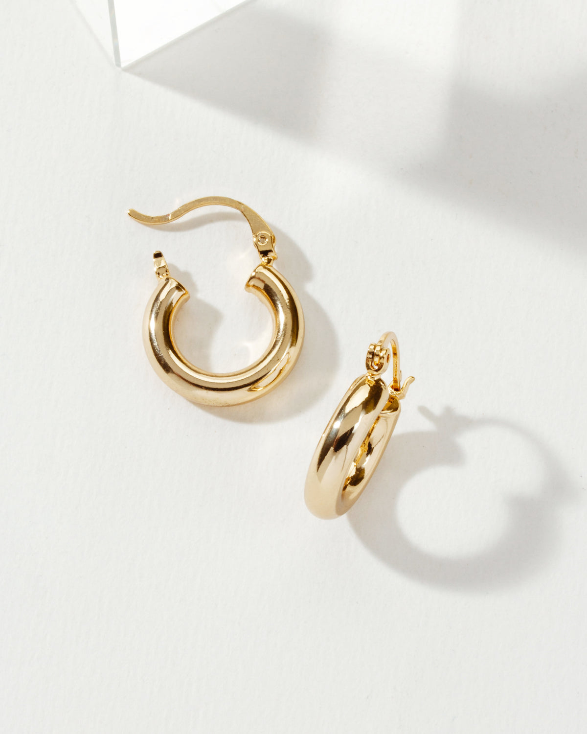 Two gold Understated Hoop Earrings are displayed on a white surface with soft lighting.