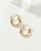 Two polished gold Understated Hoop Earrings rest on a white surface, casting subtle shadows.