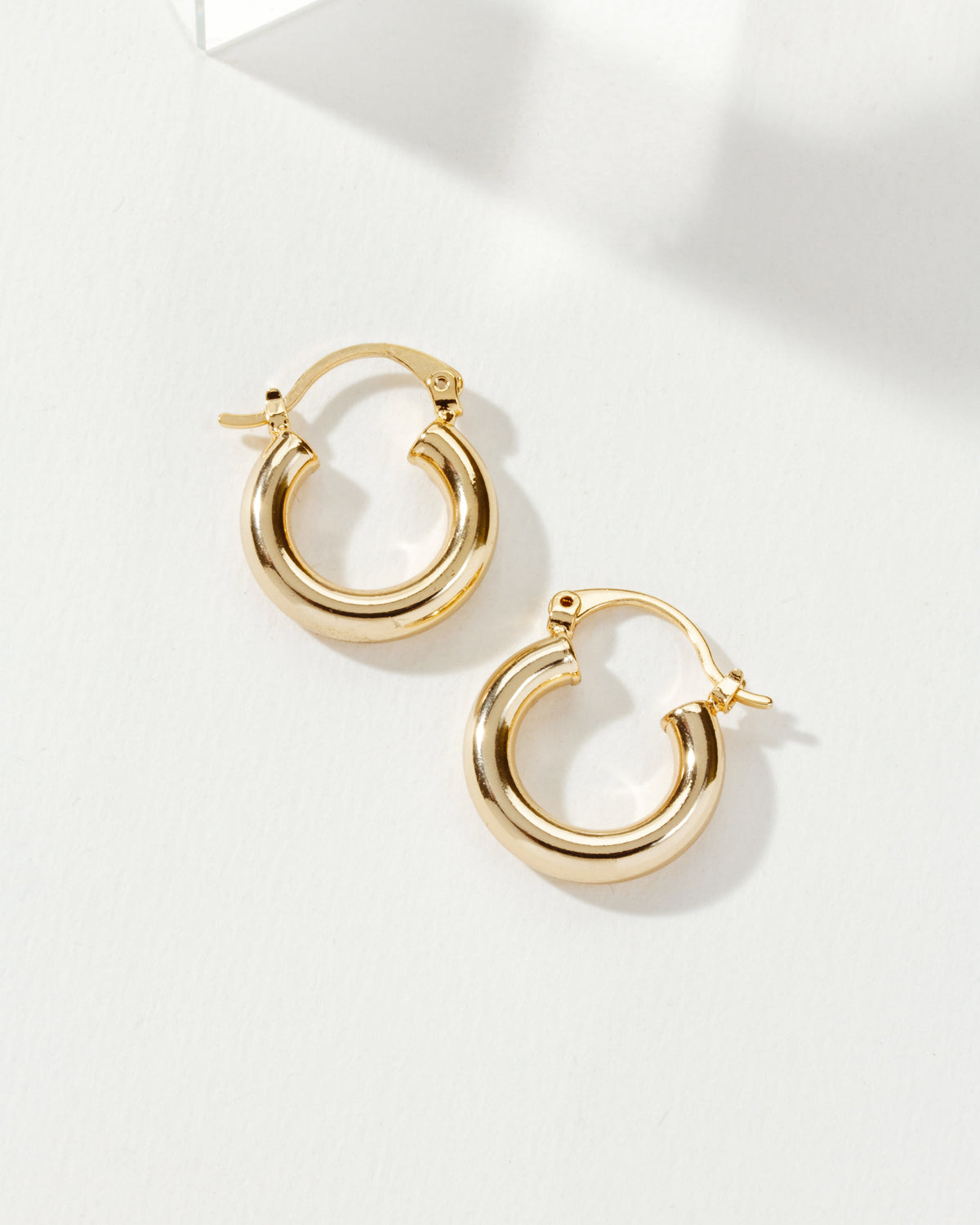 Two polished gold Understated Hoop Earrings rest on a white surface, casting subtle shadows.