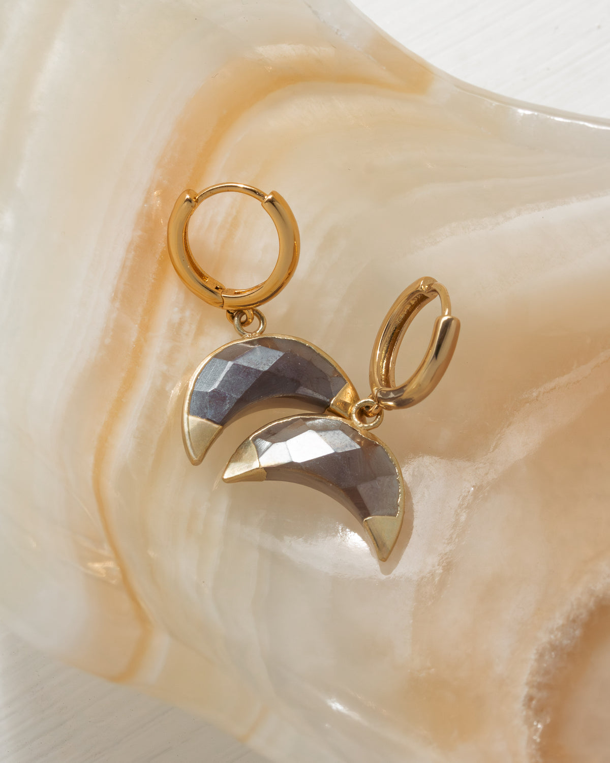 Gold earrings with half-moon designs on a stone background