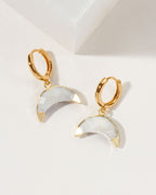 Two gold Crescent Horn Huggie Hoop Earrings with Moonstone accents are displayed on a white surface.