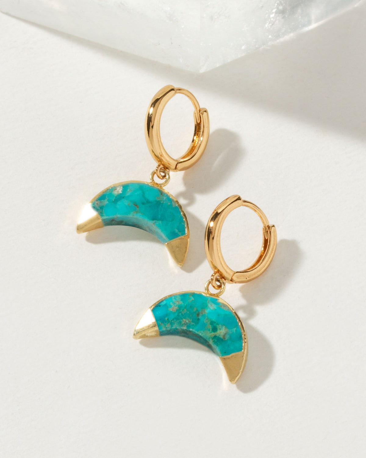 Pair of gold huggie hoop earrings with turquoise crescent horn gemstone pendants.