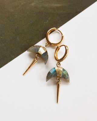 Pair of gold huggie hoop earrings with faceted Labradorite crescent horn charm and gold spike on a white and dark green background.