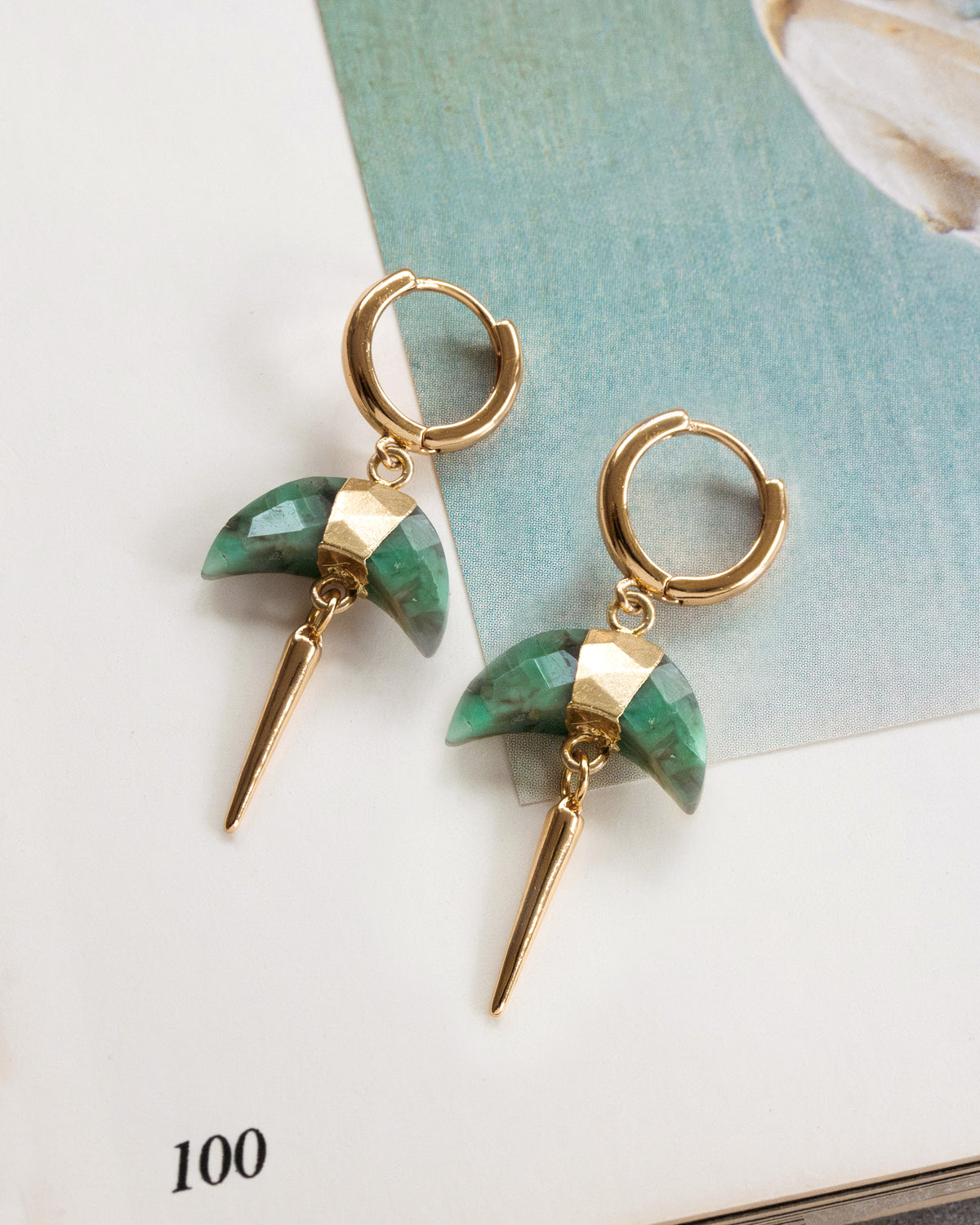 Gold crescent earrings with green stone and spike design on a light background