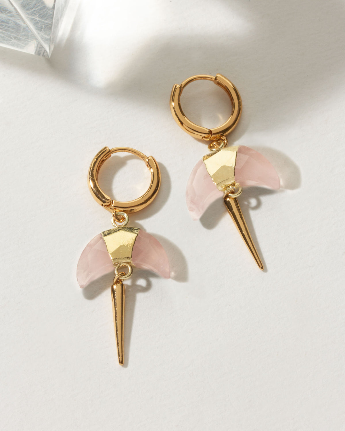 Pair of gold huggie hoop earrings with a rose quartz crescent horn charm.