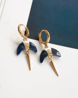Huggie hoop earrings with a Sapphire crescent horn charm and gold spike accent on a white and dark blue background.