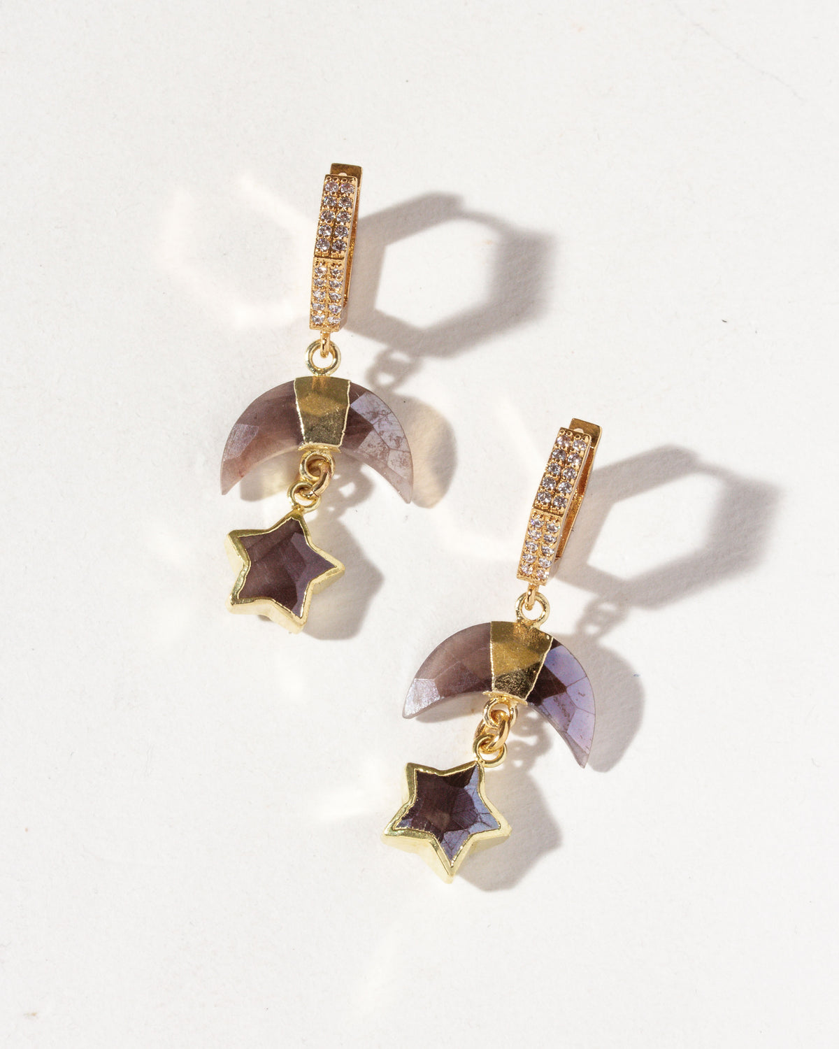 A pair of gold-colored hoop earrings with hexagon shapes encrusted with cz stones, suspended from them are coffee moonstone crescent charm with a gemstone star.