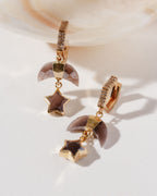 Pair of coffee moonstone earrings with coffee moonstone star and moon charms with cz elements on a white surface.