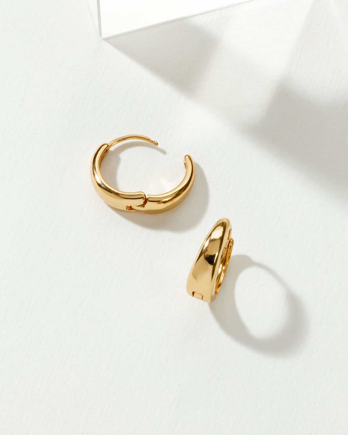 Two Elevated Huggie Hoop Earrings, with a golden plating, are displayed against a white background.