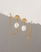 Gold earrings with pearl drops on a textured surface