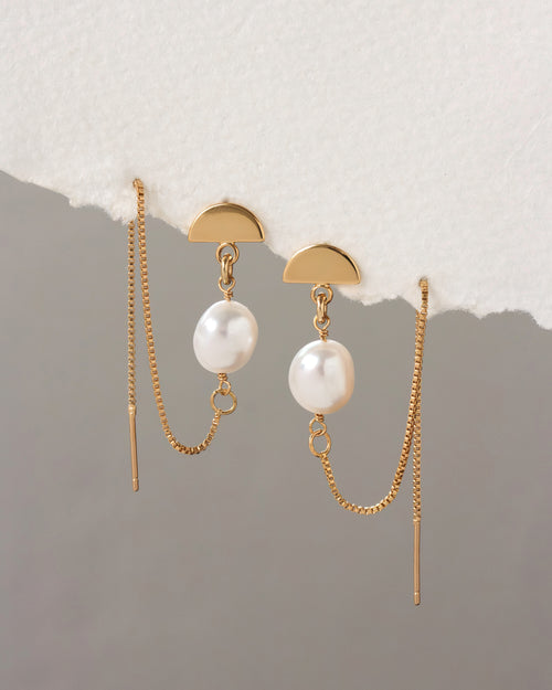 Gold earrings with pearl drops on a textured surface
