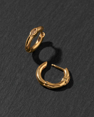 A pair of small gold huggie hoop earrings with clear CZ marquise details.