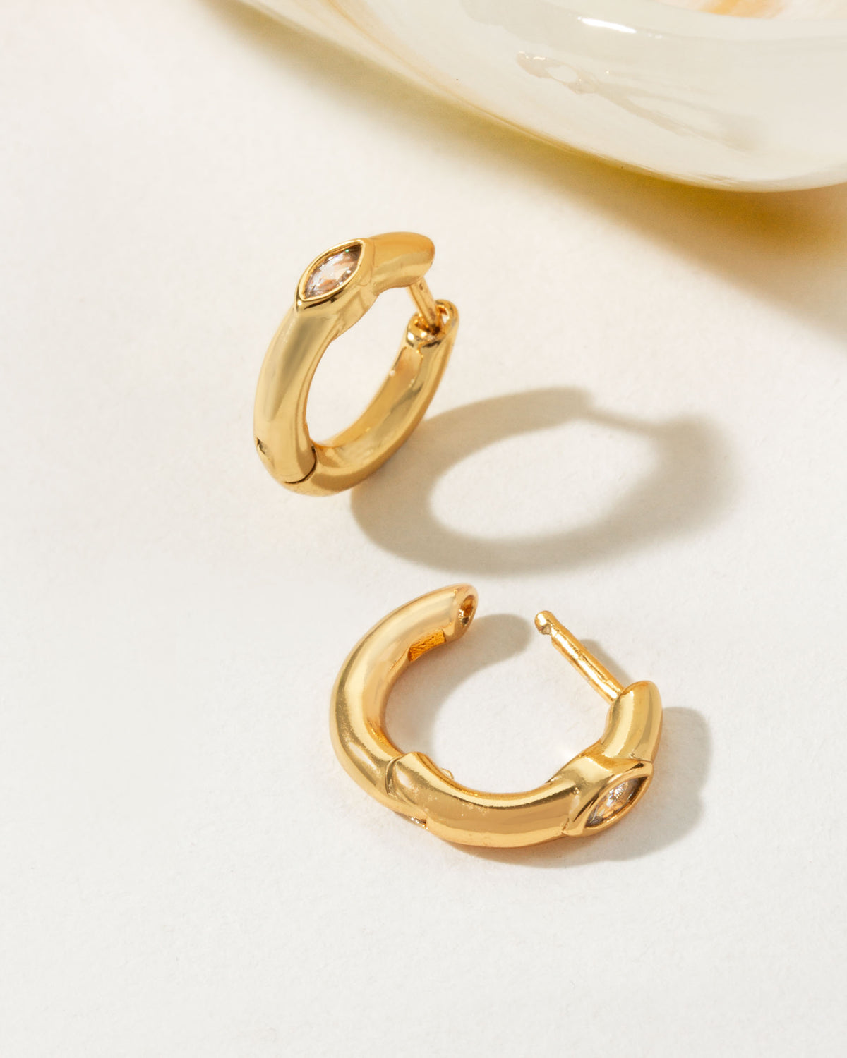 Two Golden Gaze CZ Huggie Hoop Earrings are displayed on a white surface.