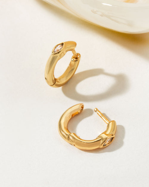 Two Golden Gaze CZ Huggie Hoop Earrings are displayed on a white surface.