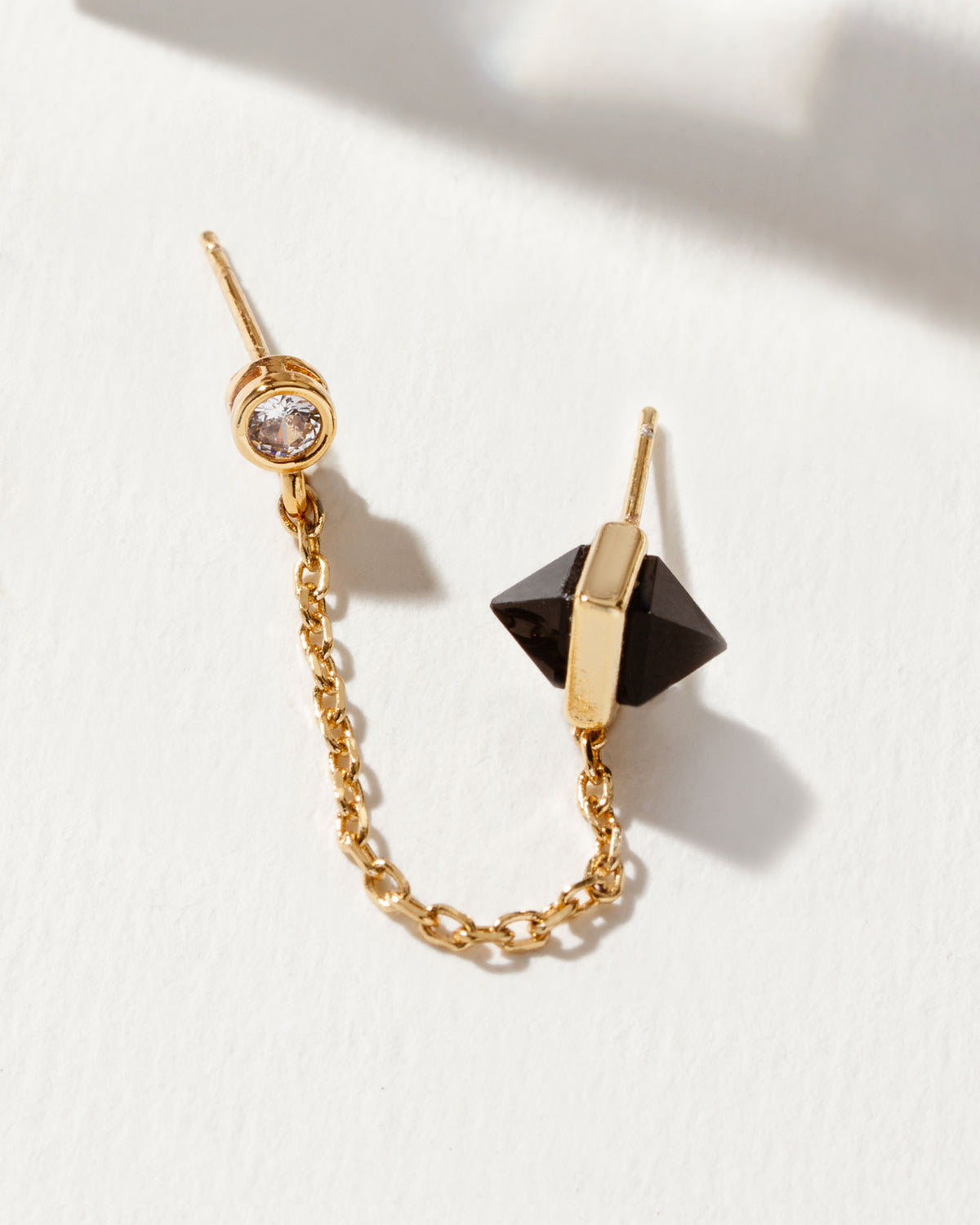 Gold double-piercing earring with crystal stud, onyx pyramids, and chain