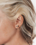 Close-up of an ear wearing a gold earring with a small round stone.