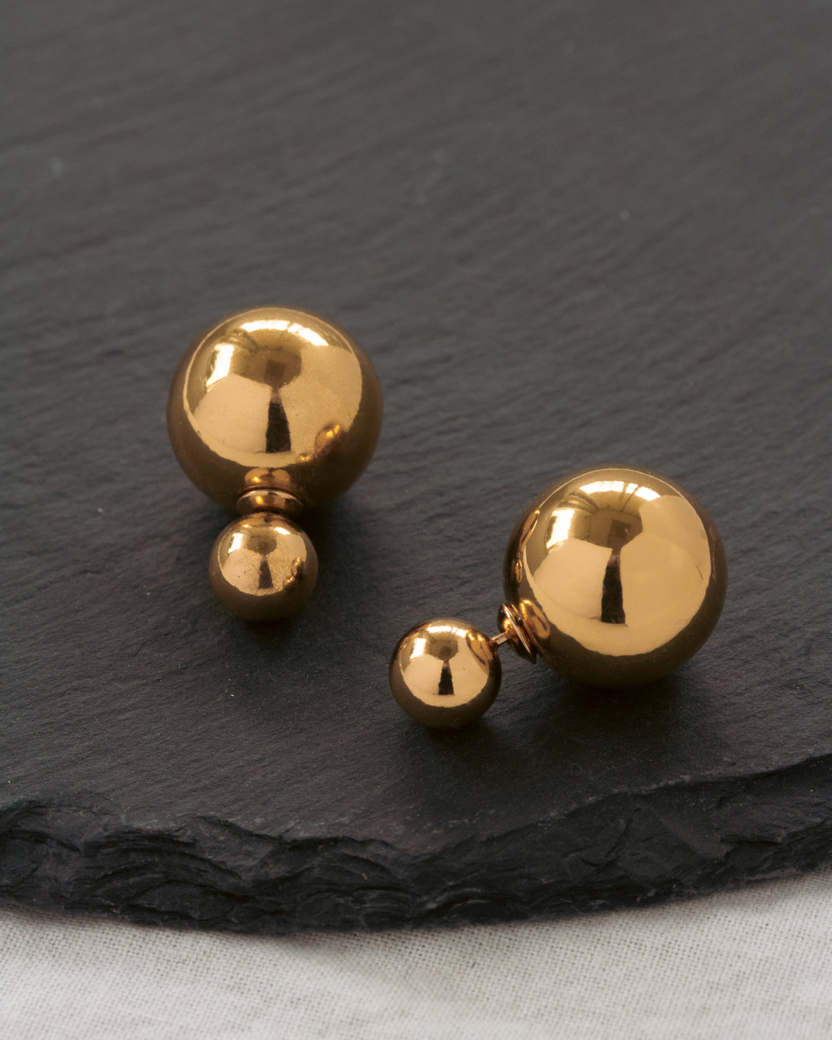 Set of gold spherical earrings on a dark slate surface