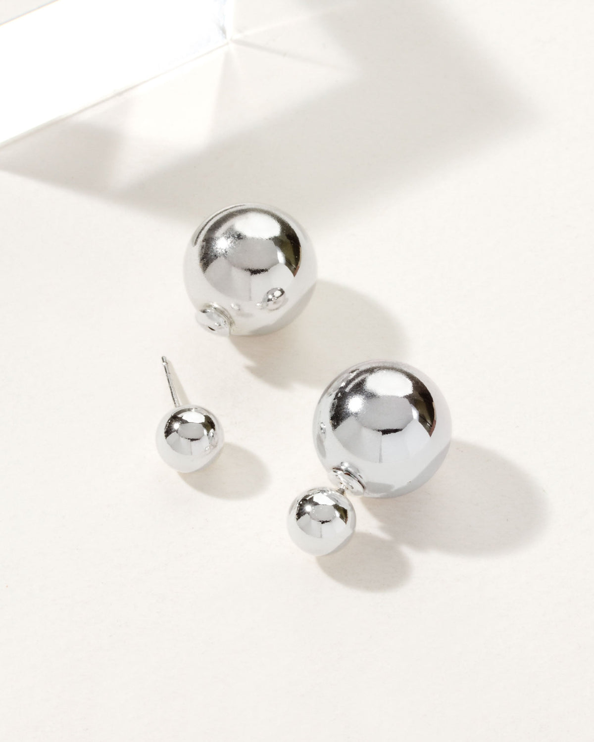 Two pairs of shiny, silver, orb-shaped earrings are displayed on a white surface.