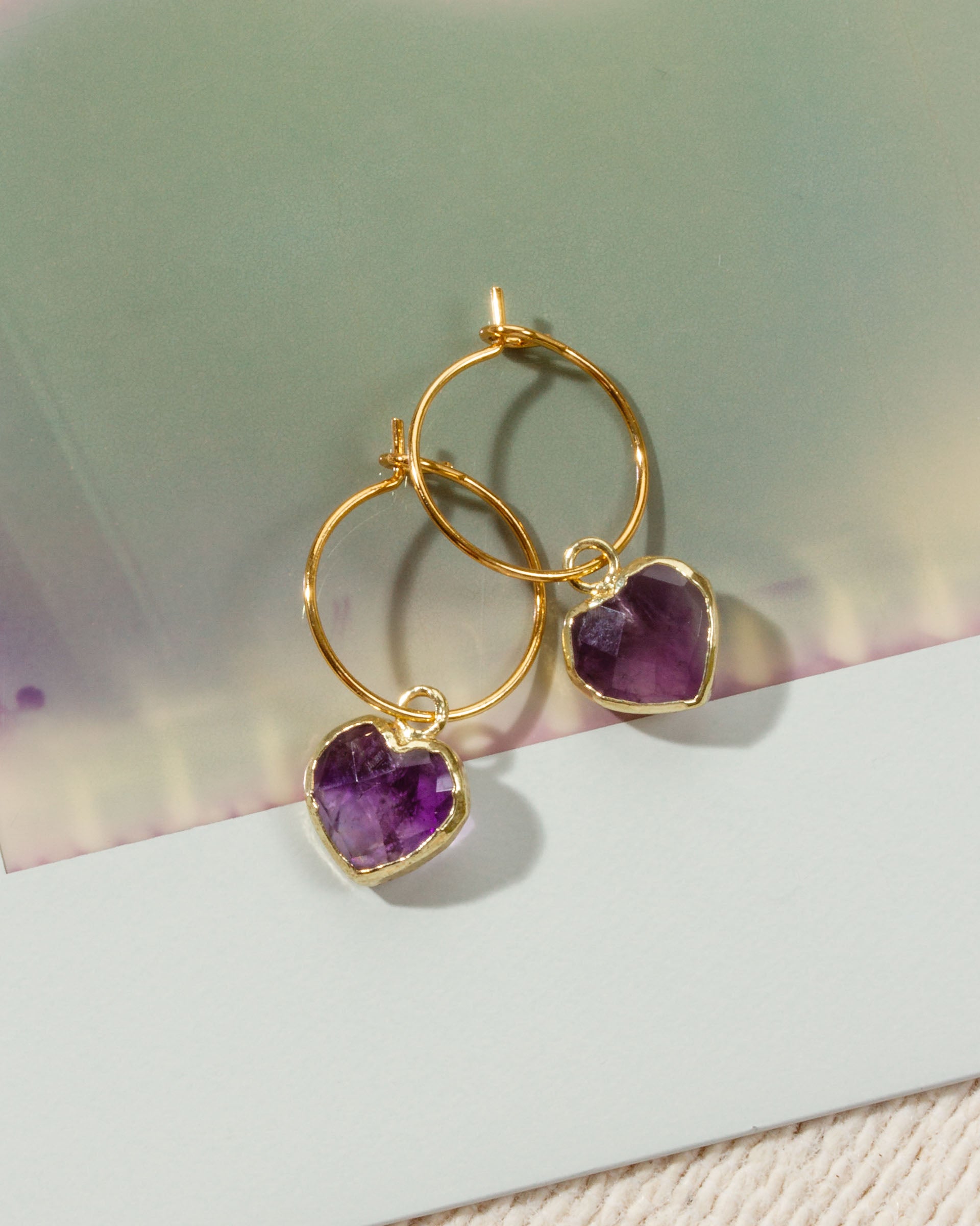 A pair of gold hoop earrings with heart-shaped purple amethyst pendants.