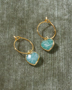 A pair of gold hoop earrings with heart-shaped light blue amazonite gemstone pendants.
