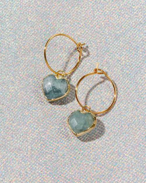Gold hoop earrings with heart-shaped light blue aquamarine gemstone charms.