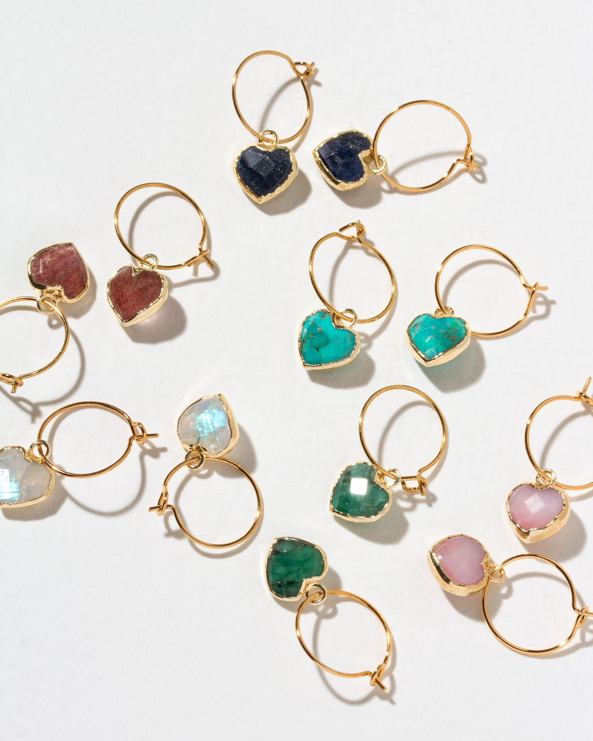 Gold hoop earrings with heart-shaped gemstone charms in multiple colors, including turquoise, emerald green, pink, purple, and dark blue.