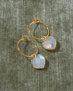 A pair of gold hoop earrings with heart-shaped iridescent moonstone drops.