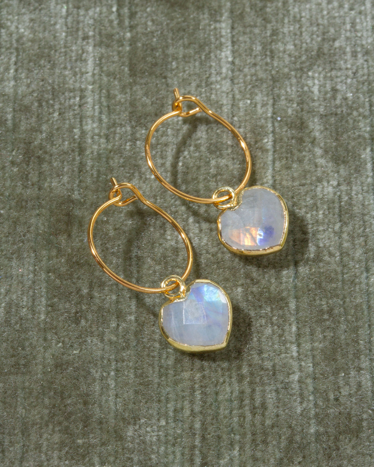 A pair of gold hoop earrings with heart-shaped iridescent moonstone drops.