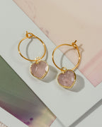 A pair of gold hoop earrings with faceted light pink rose quartz stone pendants.