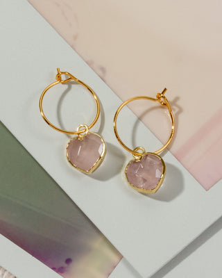 A pair of gold hoop earrings with faceted light pink rose quartz stone pendants.