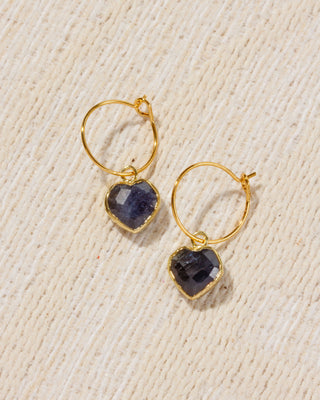 A pair of gold hoop earrings with heart-shaped dark blue sapphire gemstone charms.