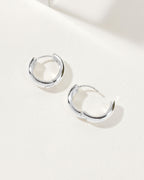Two silver Huggie Hoop Earrings displayed on a white surface in natural light.