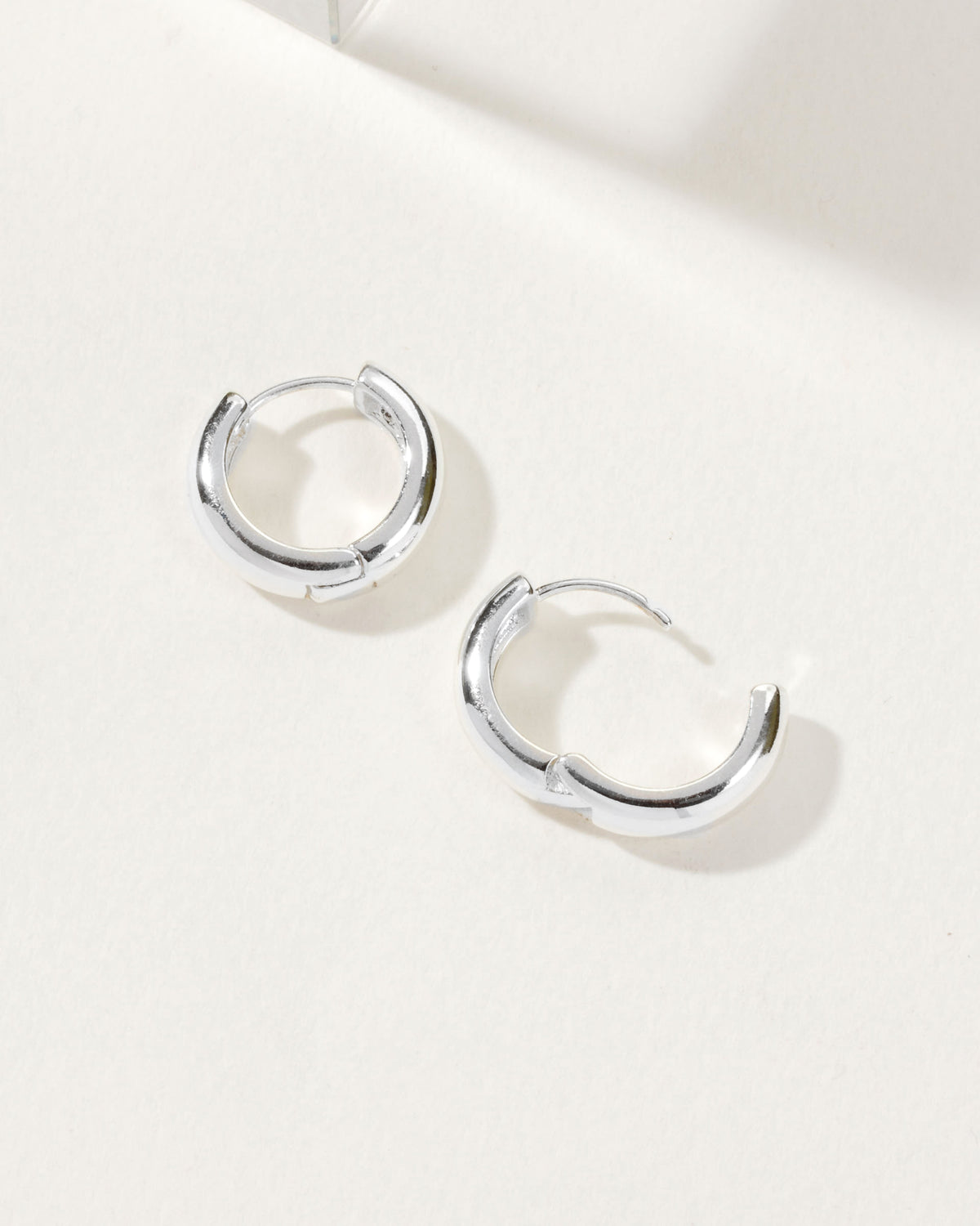 Two silver Huggie Hoop Earrings displayed on a white surface in natural light.