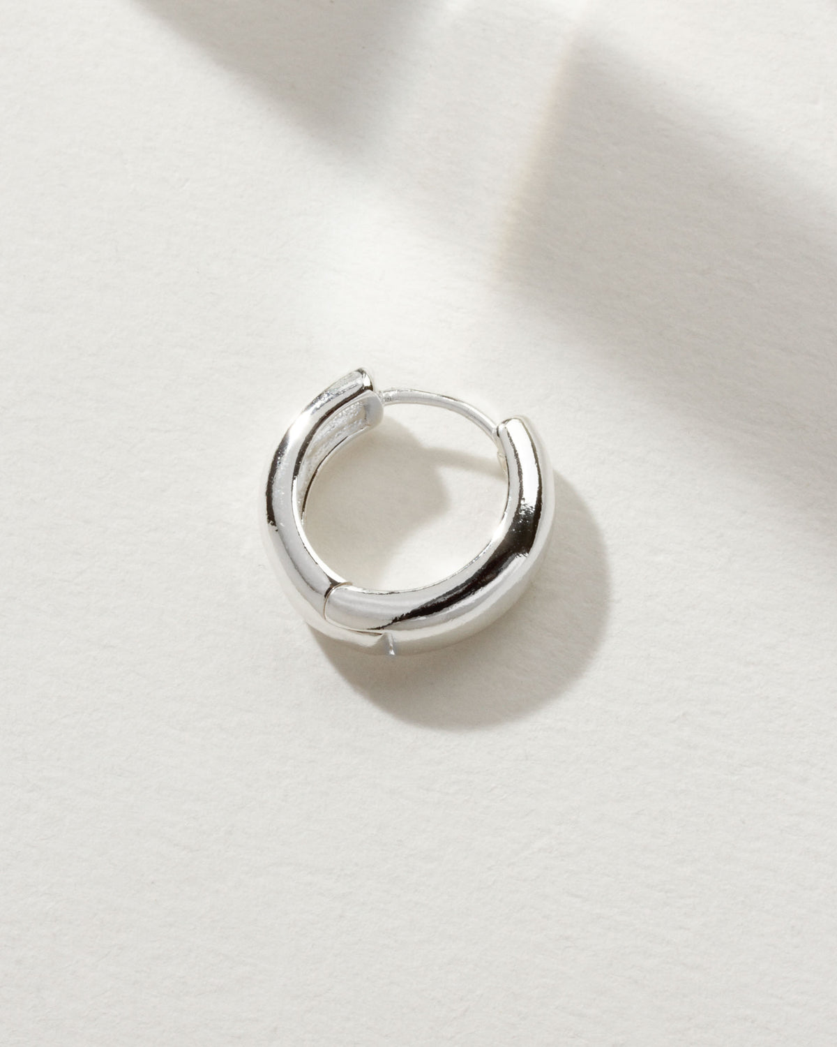 Silver huggie hoop earring on a white surface.