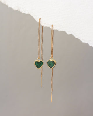 Gold heart-shaped earrings with green gemstones on a light gray background
