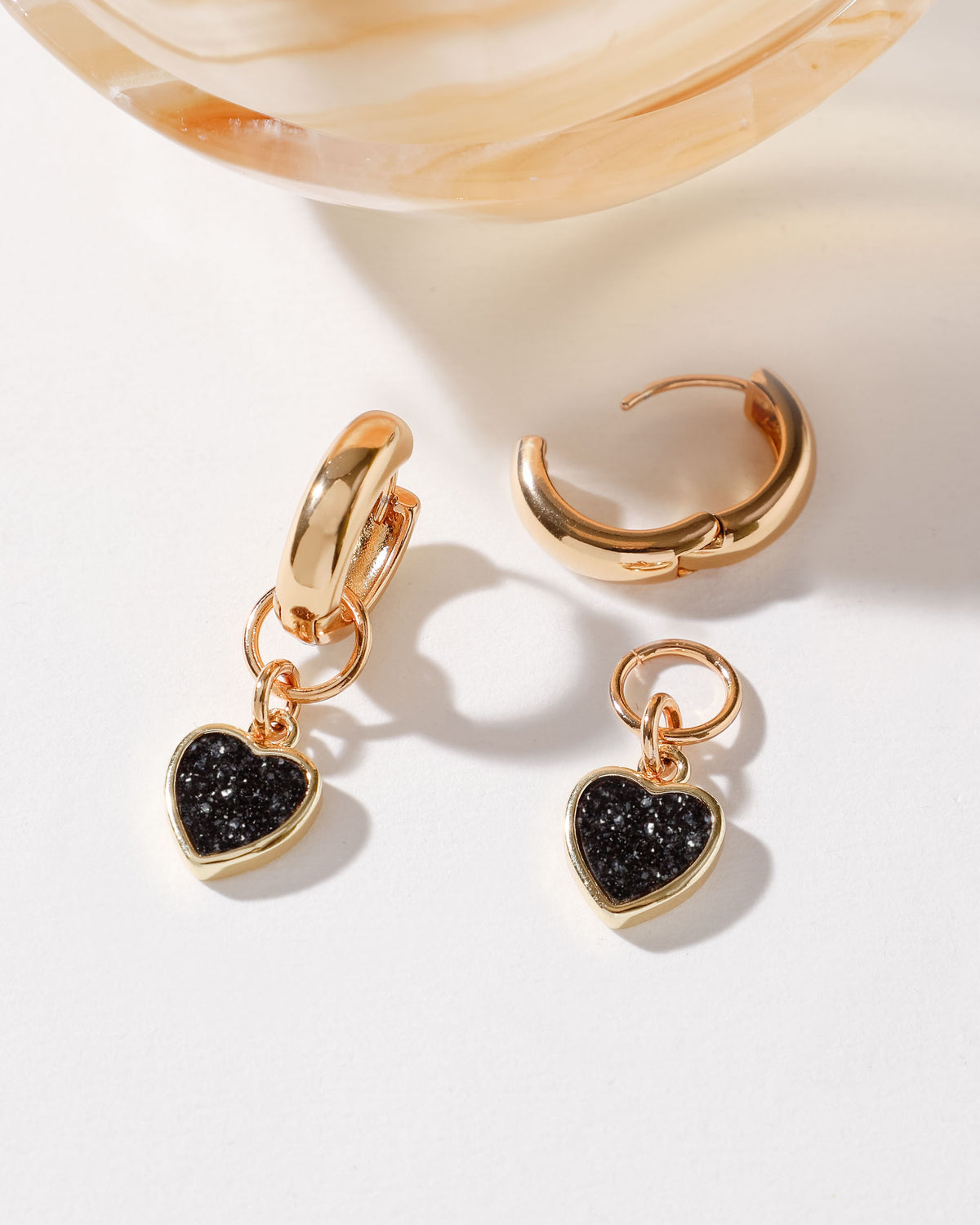 Gold huggie hoop earring with a Black Druzy heart charm.