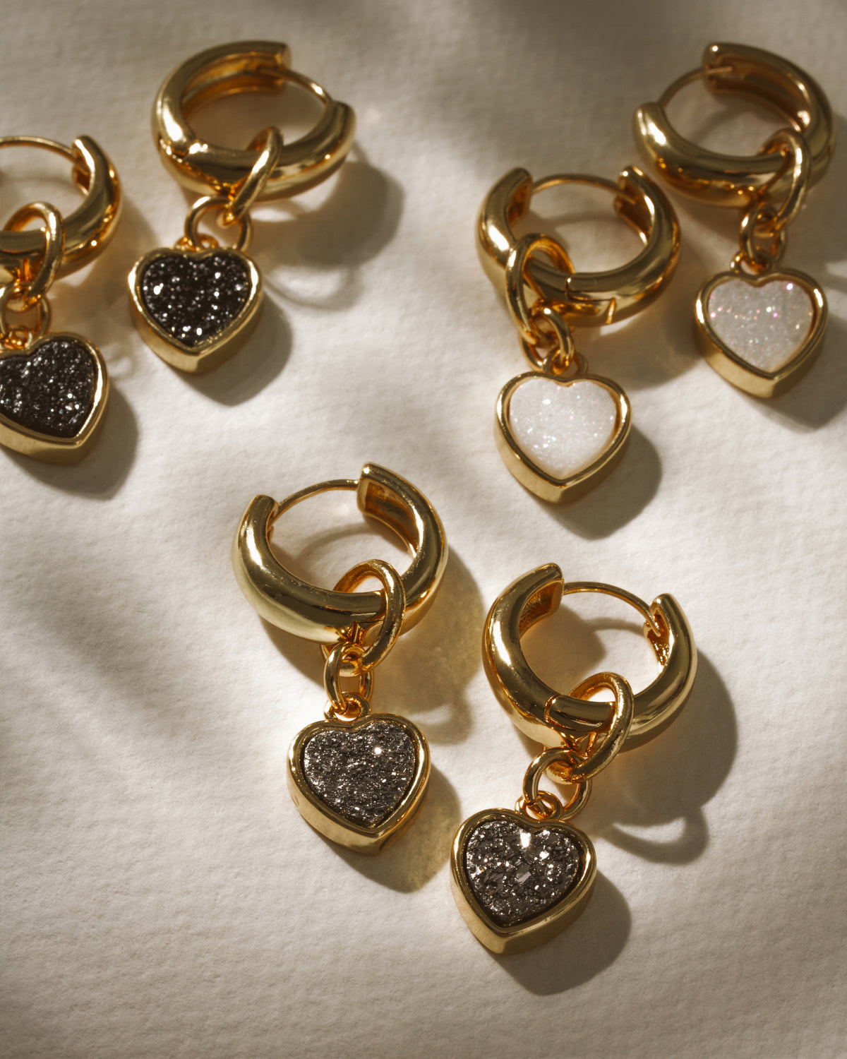 Gold huggie hoop earrings with heart charms in Black Druzy and White Druzy.