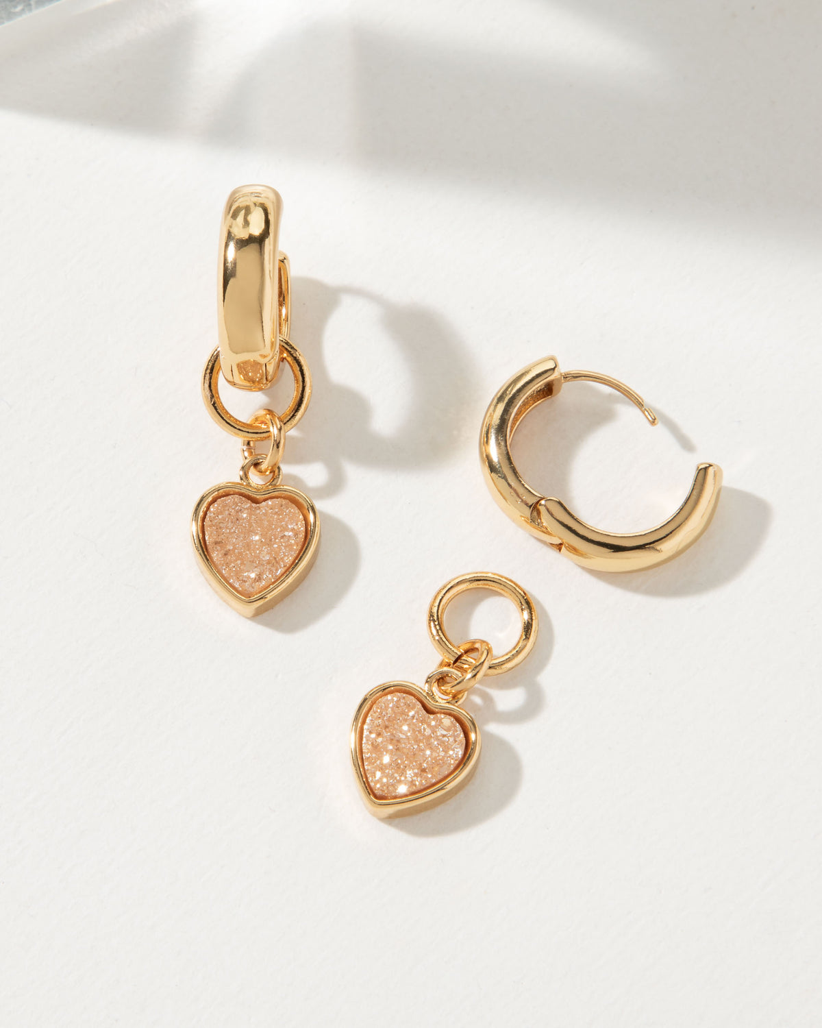 Gold huggie hoop earring with a Peach Druzy heart charm.