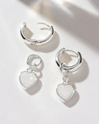Silver huggie hoop earrings with a white druzy heart charm are displayed.