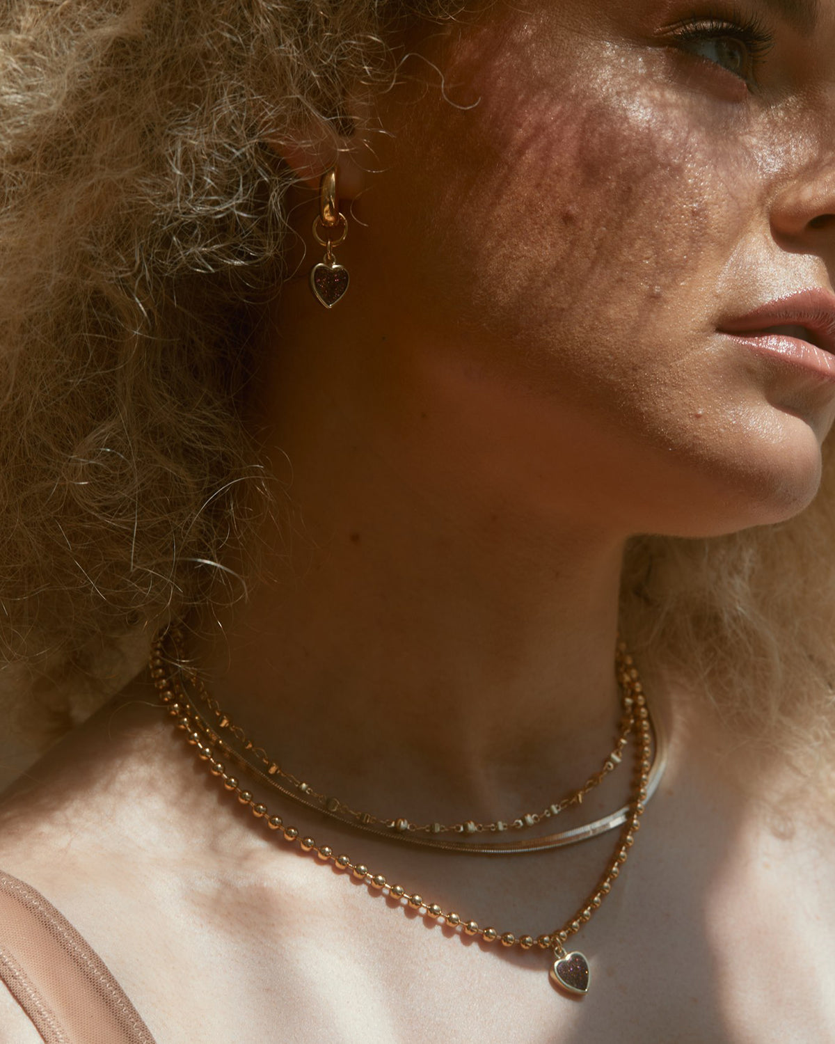 Gold huggie hoop earring with a heart charm, featuring a Plum Druzy stone.